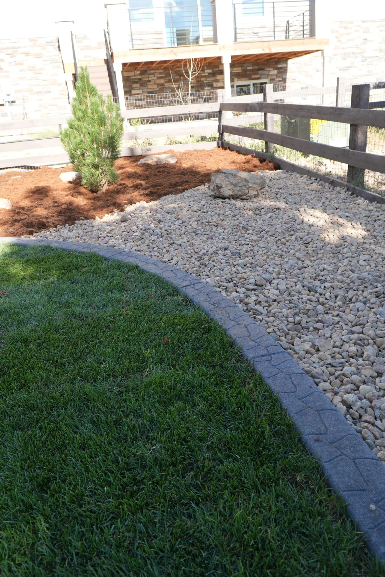Backyard lawn with concrete curbing and river rock bed by Calaway Sprinkler